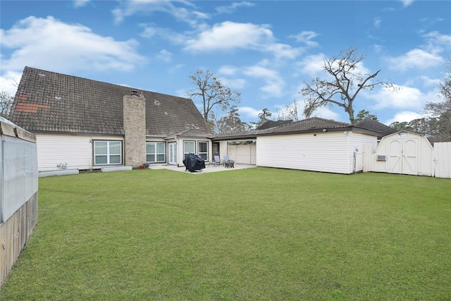rear view of house featuring an outdoor structure, a chimney, a storage unit, a patio area, and a yard