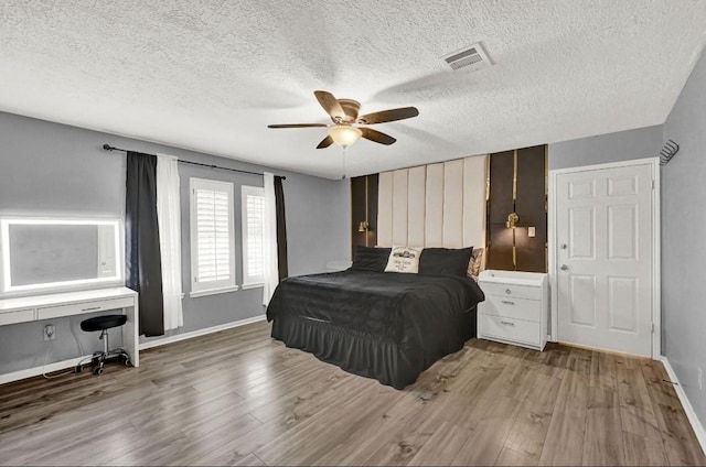 bedroom featuring visible vents, wood finished floors, baseboards, a textured ceiling, and a ceiling fan