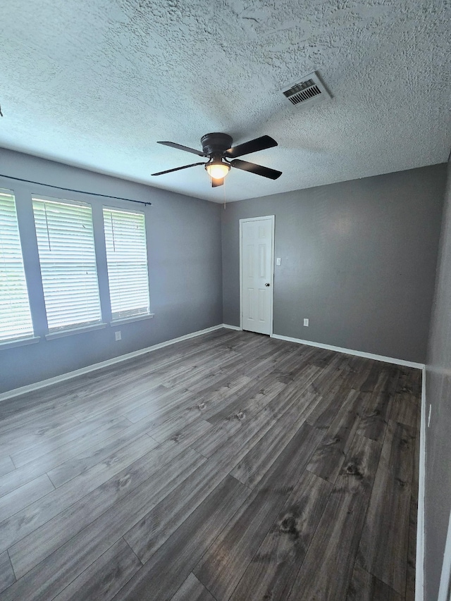 spare room with dark wood-style flooring, a textured ceiling, a ceiling fan, baseboards, and visible vents