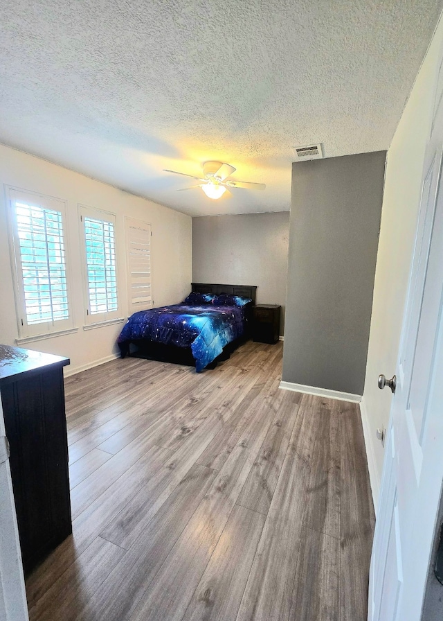 bedroom featuring a ceiling fan, a textured ceiling, visible vents, wood finished floors, and baseboards