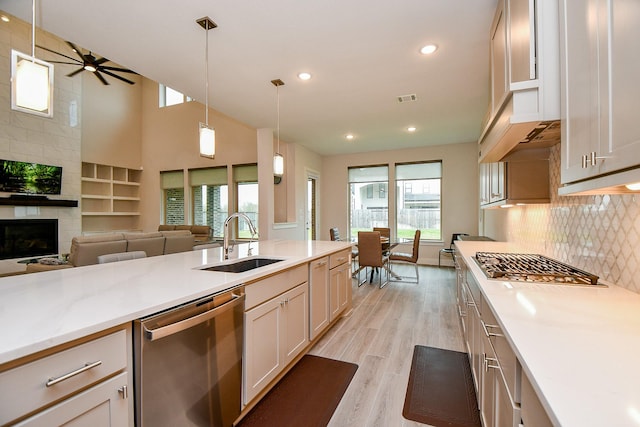 kitchen with a fireplace, a sink, stainless steel dishwasher, decorative backsplash, and light wood finished floors