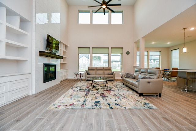 living room with a tiled fireplace, wood finished floors, a ceiling fan, and baseboards