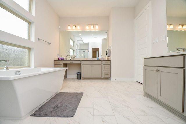 bathroom featuring marble finish floor, two vanities, a freestanding tub, and baseboards