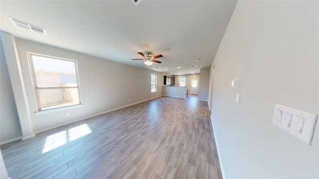 unfurnished living room with a ceiling fan, light wood-type flooring, visible vents, and baseboards