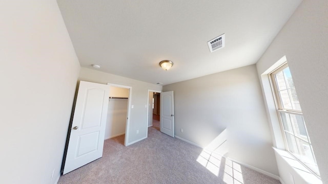 unfurnished bedroom with light colored carpet, a walk in closet, visible vents, and baseboards