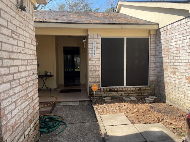 property entrance with roof with shingles and brick siding