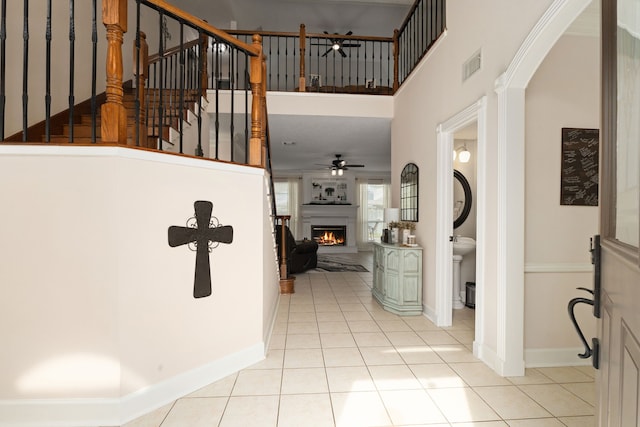 foyer with light tile patterned floors, visible vents, a towering ceiling, baseboards, and a lit fireplace