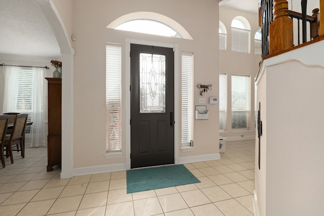 entryway with a towering ceiling, light tile patterned floors, baseboards, and arched walkways