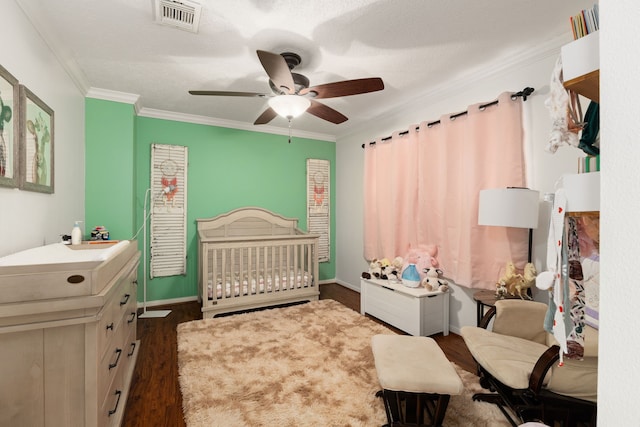 bedroom featuring crown molding, dark wood finished floors, visible vents, ceiling fan, and a crib