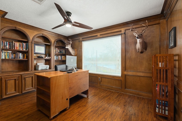 home office with a textured ceiling, wooden walls, a ceiling fan, dark wood-style floors, and crown molding