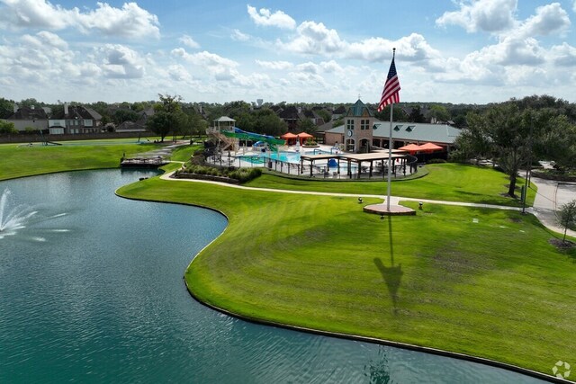 view of community featuring a water view, a lawn, and a pool