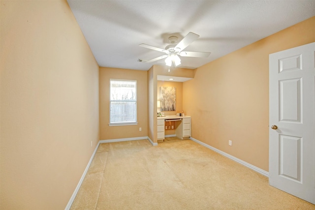 unfurnished room featuring baseboards, light carpet, ceiling fan, and built in study area