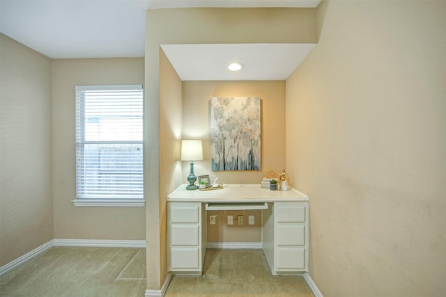 office area featuring light colored carpet, baseboards, and built in desk