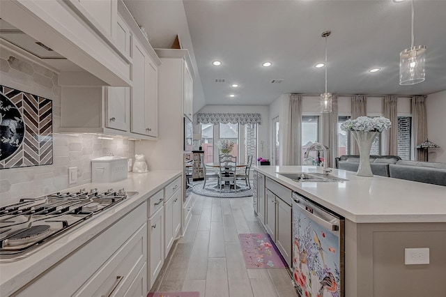 kitchen with appliances with stainless steel finishes, light countertops, a sink, and wall chimney range hood