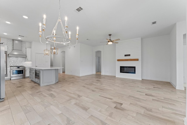 unfurnished living room featuring arched walkways, a large fireplace, ceiling fan with notable chandelier, visible vents, and light wood finished floors