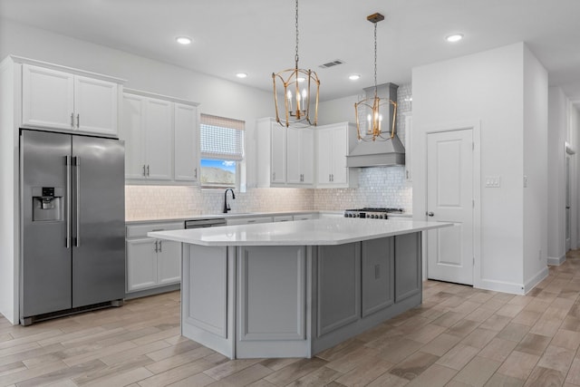 kitchen featuring high end refrigerator, a kitchen island, visible vents, light countertops, and wall chimney range hood