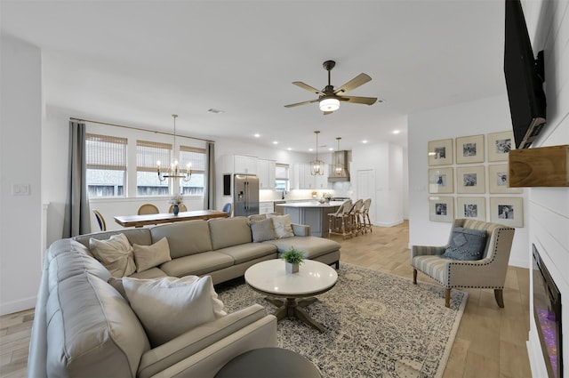 living room with a fireplace, recessed lighting, light wood-style flooring, baseboards, and ceiling fan with notable chandelier