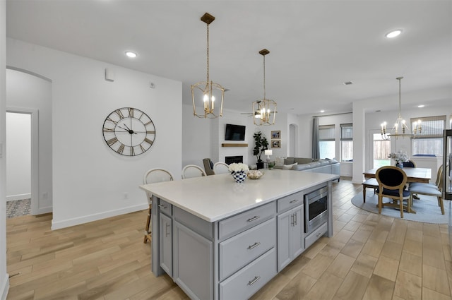 kitchen with stainless steel microwave, open floor plan, gray cabinets, a fireplace, and a notable chandelier