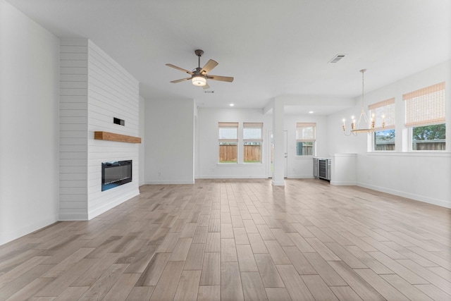 unfurnished living room with a fireplace, visible vents, light wood-style floors, baseboards, and ceiling fan with notable chandelier