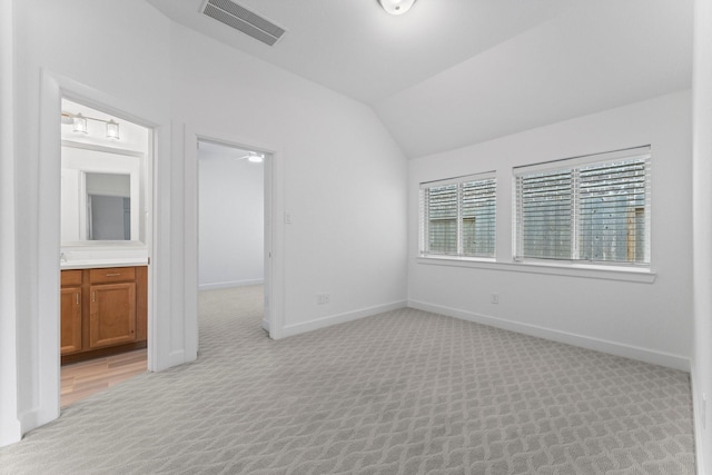 empty room with light carpet, vaulted ceiling, visible vents, and baseboards