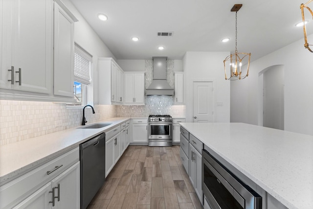 kitchen with tasteful backsplash, appliances with stainless steel finishes, white cabinets, a sink, and wall chimney range hood