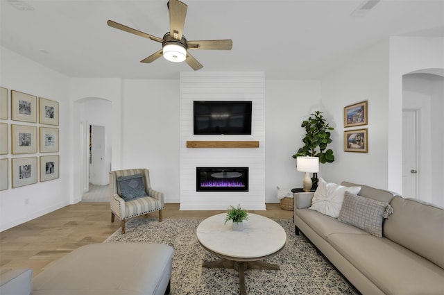 living room with arched walkways, a fireplace, visible vents, a ceiling fan, and wood finished floors