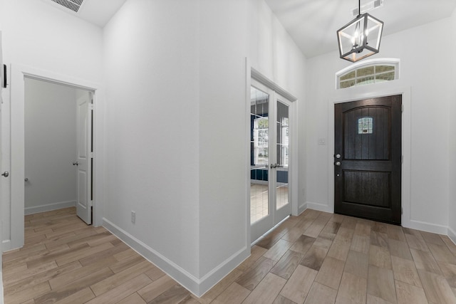 foyer entrance with a notable chandelier, visible vents, light wood-style flooring, a high ceiling, and baseboards