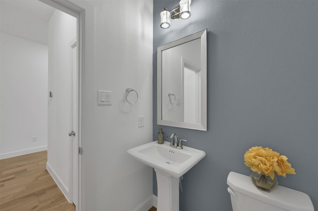 half bath featuring a sink, wood finished floors, toilet, and baseboards