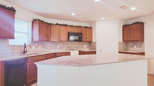 kitchen featuring visible vents, a center island, light stone countertops, black appliances, and a sink