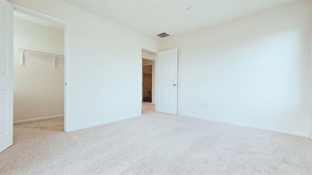 unfurnished bedroom with a walk in closet, baseboards, visible vents, and carpet flooring