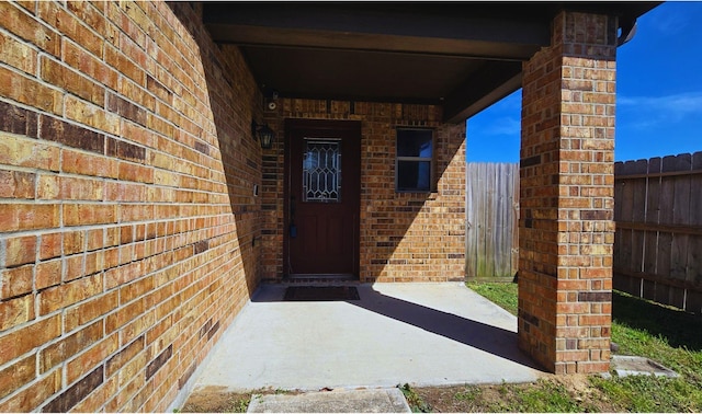 view of exterior entry with brick siding and fence