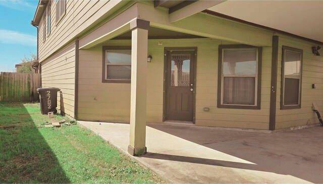 view of exterior entry featuring a lawn, a patio area, and fence