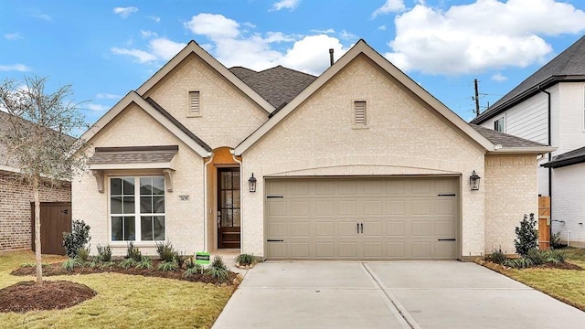 french country style house featuring concrete driveway, a shingled roof, an attached garage, and brick siding