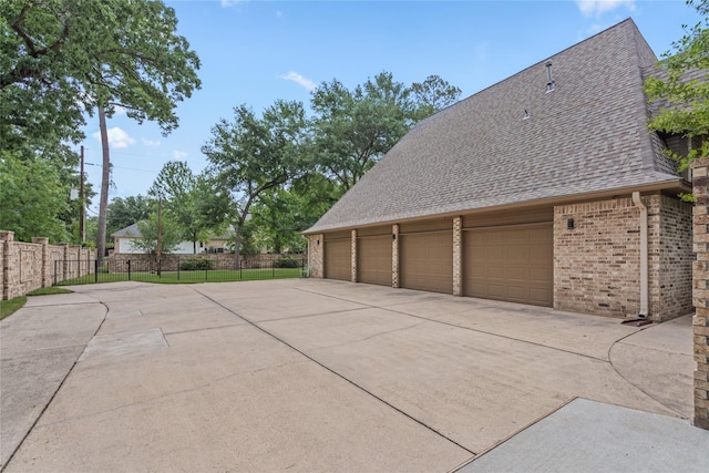 view of property exterior featuring brick siding, a detached garage, roof with shingles, and fence