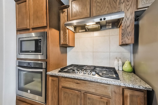 kitchen featuring appliances with stainless steel finishes, decorative backsplash, ventilation hood, and light stone countertops