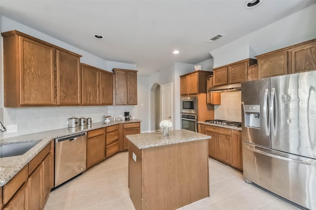 kitchen with arched walkways, a sink, appliances with stainless steel finishes, backsplash, and a center island