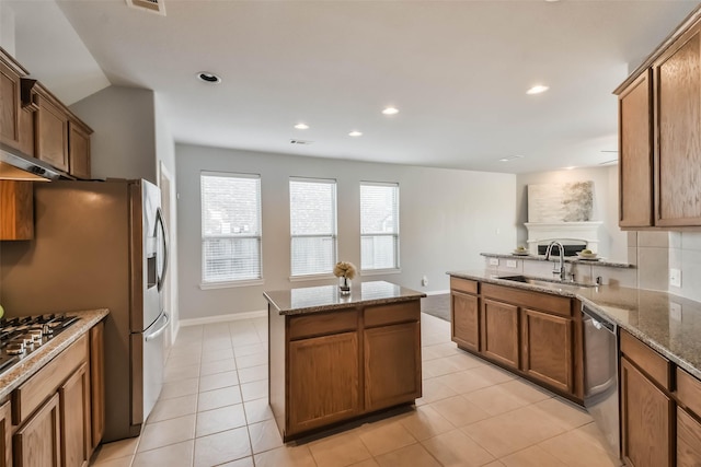 kitchen featuring stone countertops, brown cabinetry, appliances with stainless steel finishes, a center island, and a sink