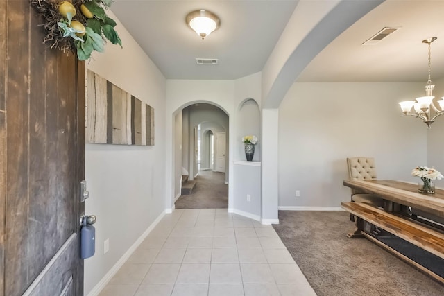 hallway featuring arched walkways, an inviting chandelier, visible vents, and light colored carpet