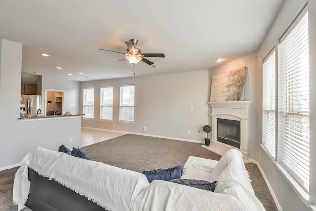 carpeted living room featuring a fireplace with raised hearth, recessed lighting, a ceiling fan, and baseboards