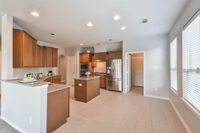 kitchen featuring visible vents, brown cabinetry, arched walkways, appliances with stainless steel finishes, and light stone counters