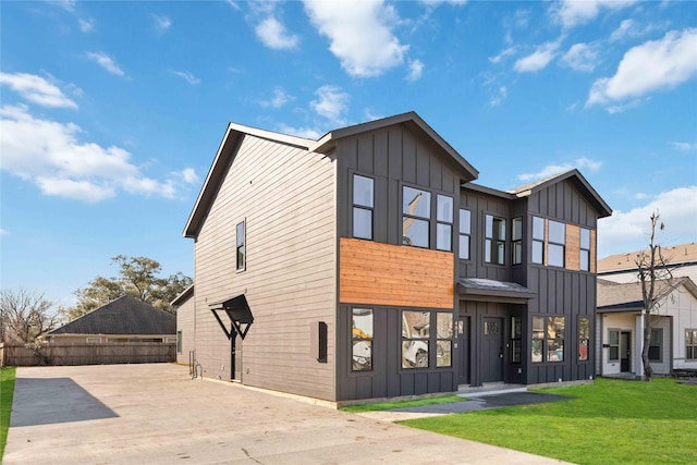 view of front of house with board and batten siding, a front yard, and fence