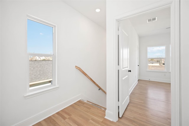 hallway with light wood-type flooring, baseboards, visible vents, and an upstairs landing