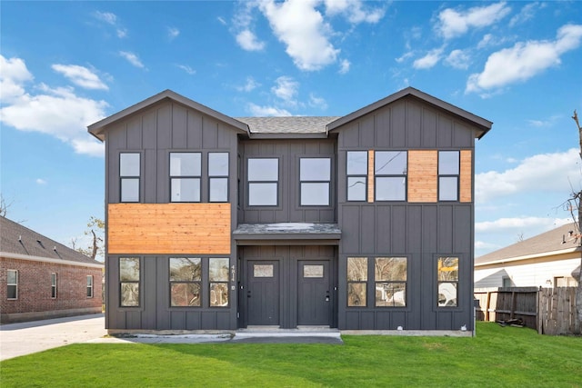 view of front of home with roof with shingles, board and batten siding, a front yard, and fence