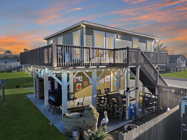 back of house at dusk featuring a patio, a lawn, stairway, and fence