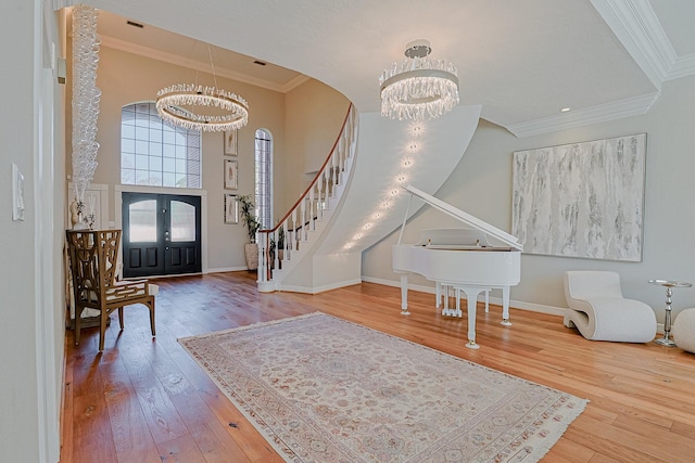 foyer entrance featuring a notable chandelier, hardwood / wood-style floors, ornamental molding, baseboards, and stairs