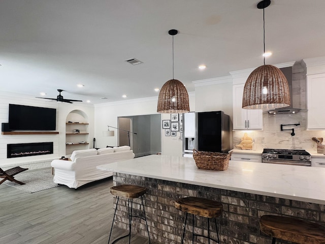 kitchen with visible vents, white cabinets, gas range, wall chimney exhaust hood, and crown molding