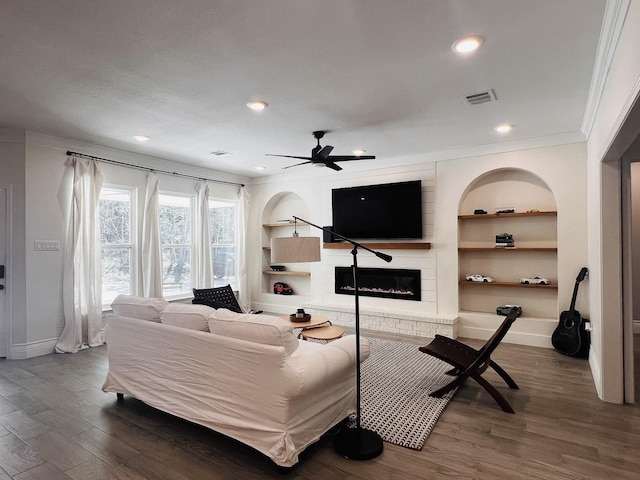 living area with built in shelves, a glass covered fireplace, visible vents, and wood finished floors