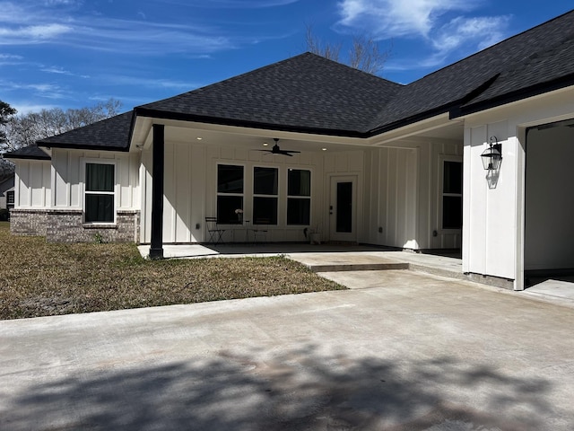 rear view of house featuring roof with shingles, a patio, brick siding, board and batten siding, and a ceiling fan