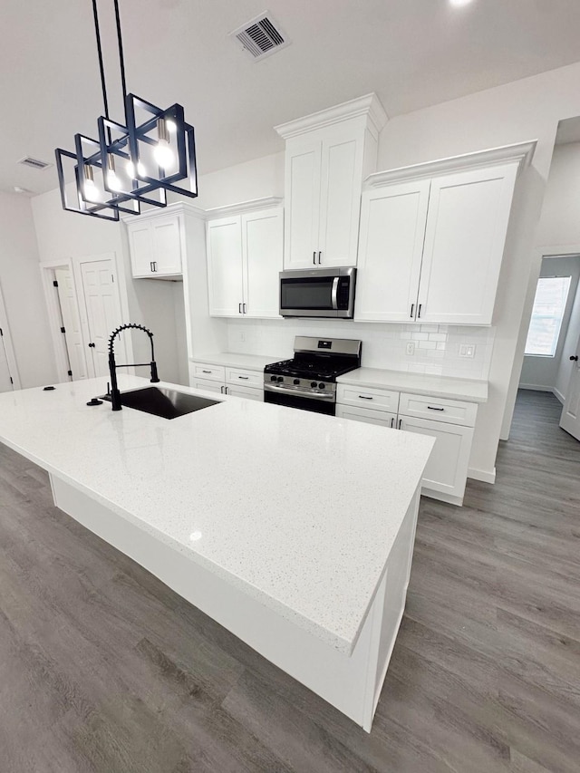 kitchen with a spacious island, visible vents, appliances with stainless steel finishes, white cabinets, and a sink