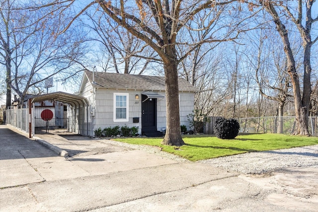 view of front of property with a detached carport, a shingled roof, fence, a front yard, and driveway